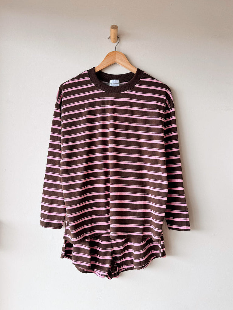 Striped long-sleeve shirt hanging on a wooden hanger against a white wall.