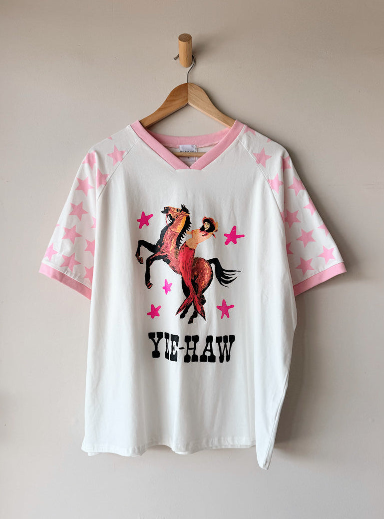 White t-shirt with a horse graphic and 'Yee-Haw' text on a hanger against a beige wall.